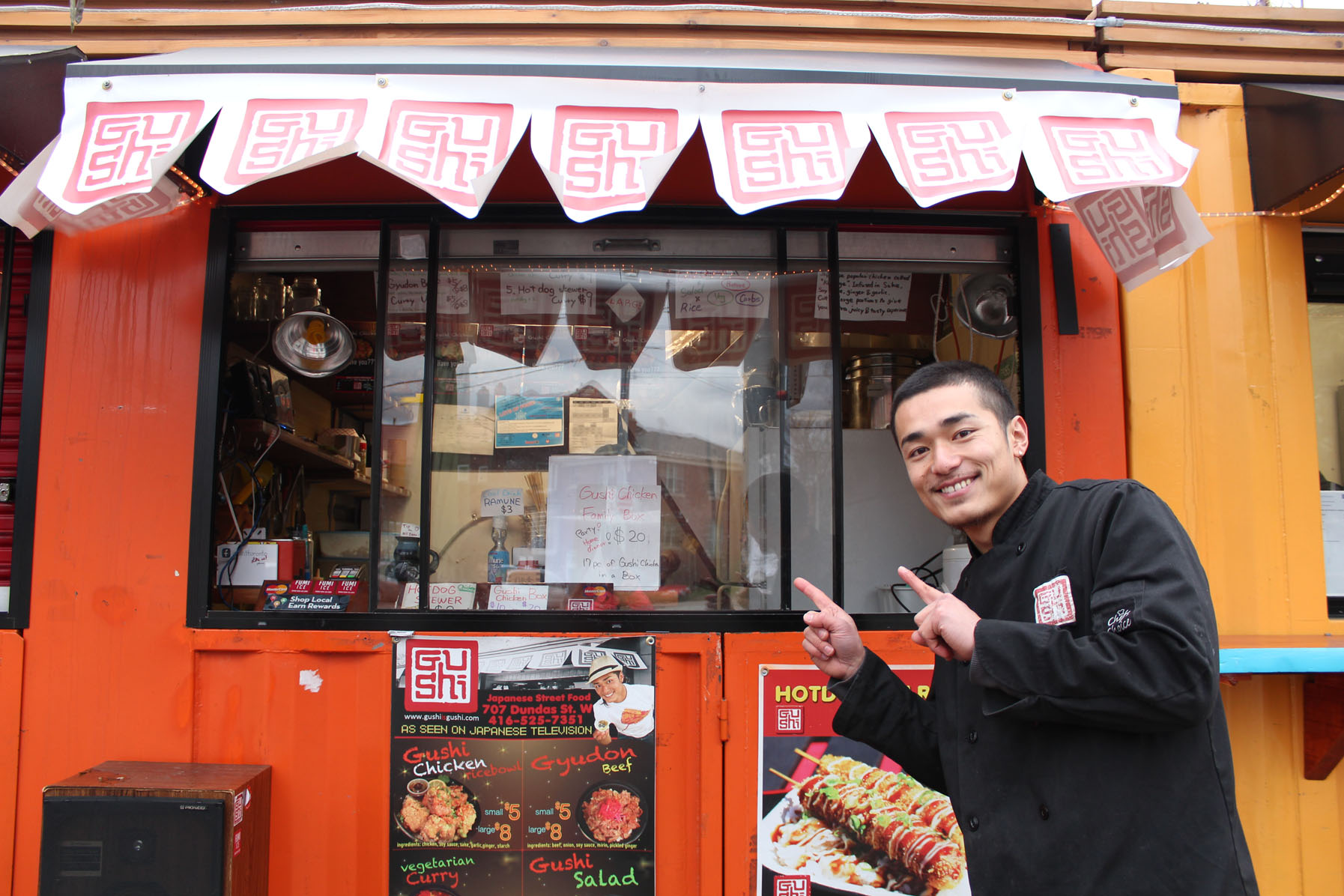 A photograph of Gushi owner Shinji-Yamaguchi in front of his stall in downtown Toronto.